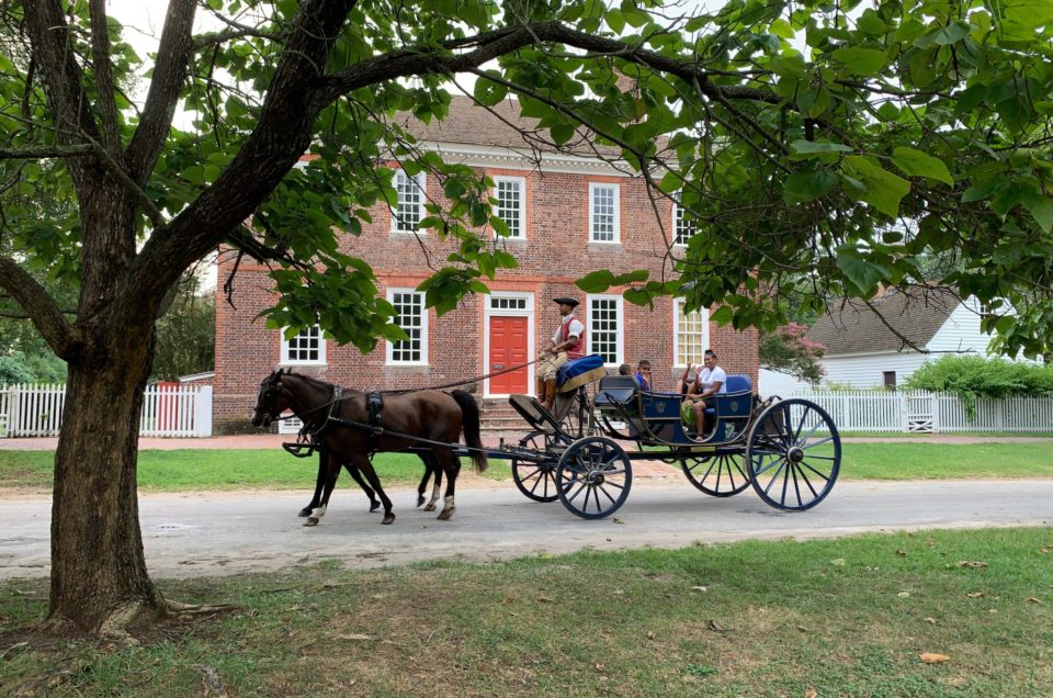 A horse-drawn carriage is driven in front of the George Wythe House in Colonial Williamsburg. We can see the head of the driver.