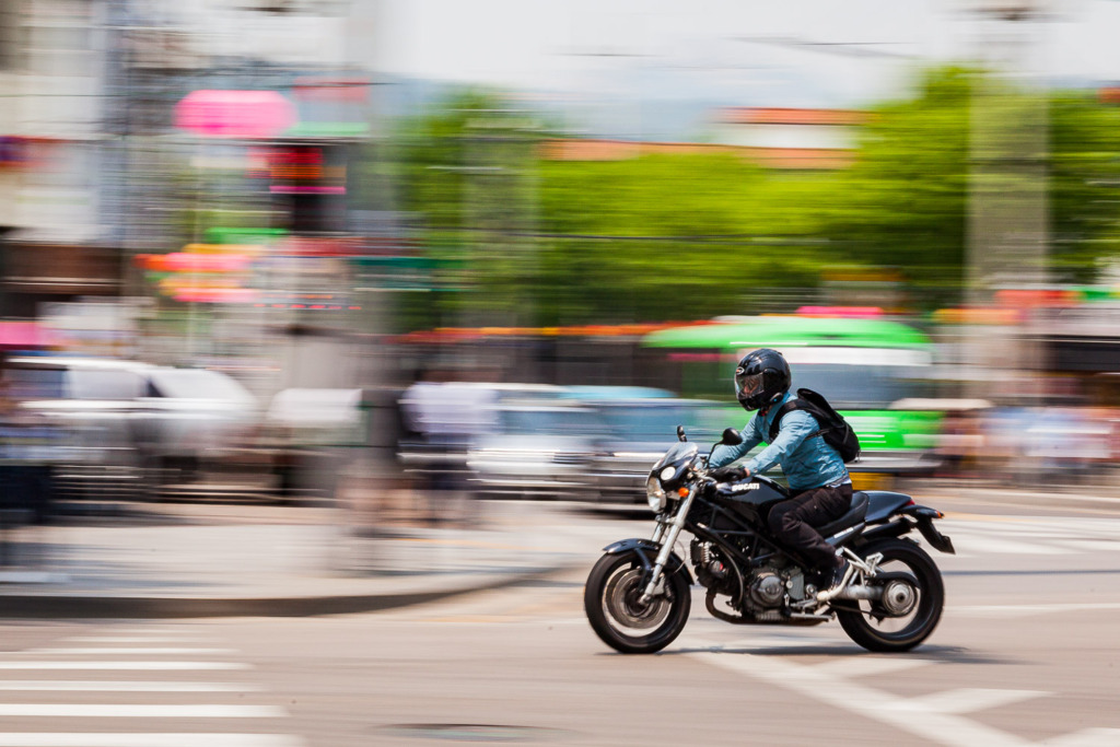 Add movement to your travel photo by panning your camera as a man rides by on a motorcycle in Seoul, South Korea.