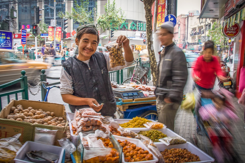 Photo of a street vendor selling nuts in Shanghai, China, as traffic and people rush by.