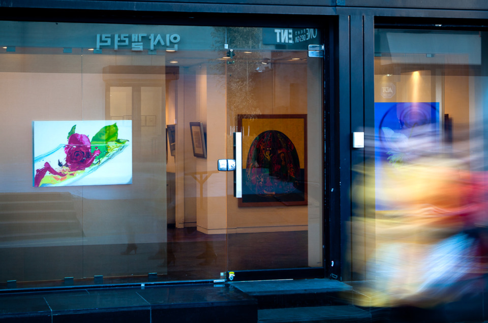 Long exposure photo of the window of an art galley in Seoul, South Korea with 3 women walking by.