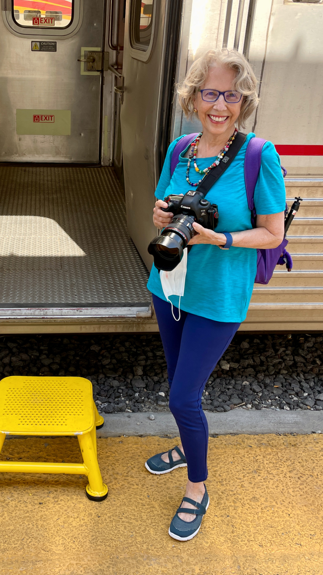 Woman standing in front of Amtrak Sleeper Car with camera in her hand and wearing a small backpack.