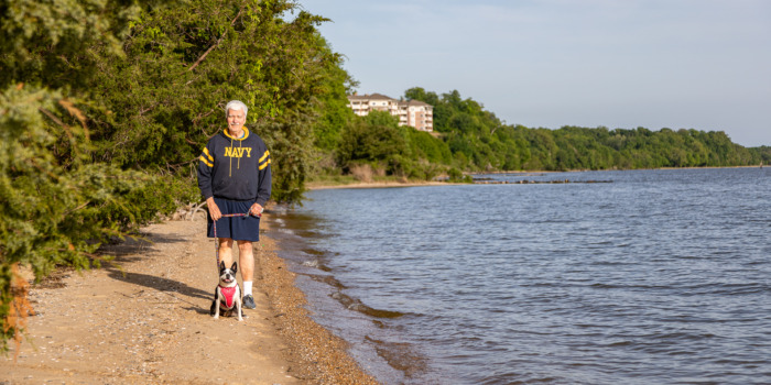 Man standing on narrow beach with his Boston Terrier.