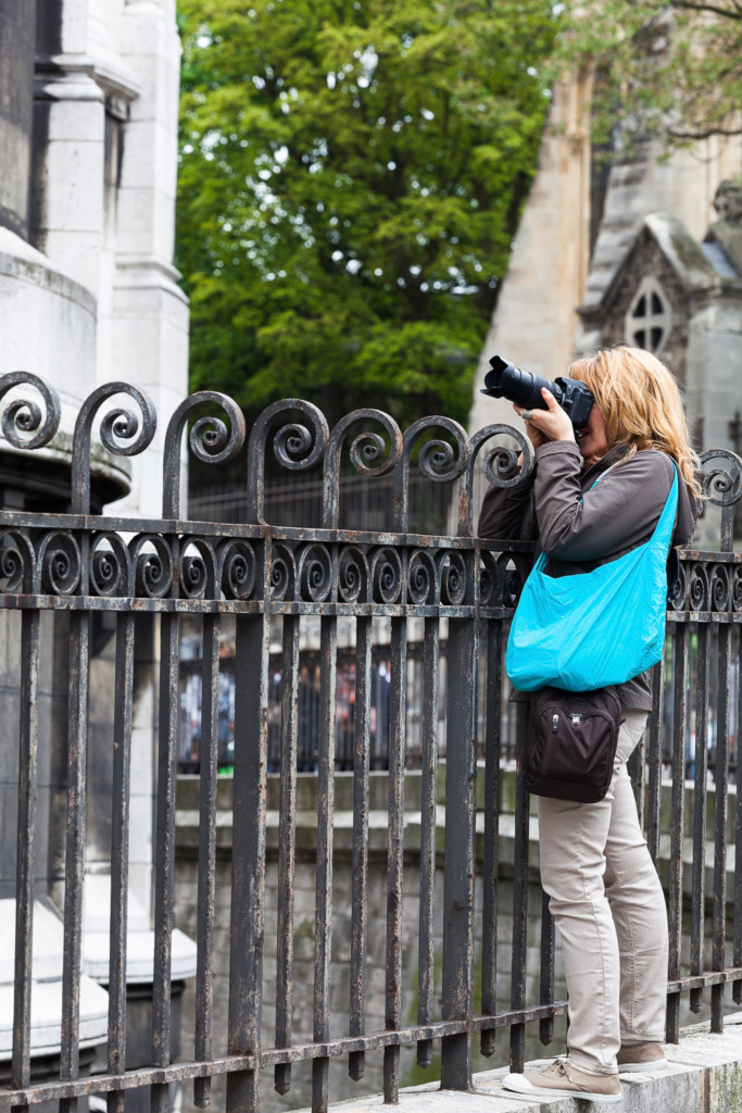 A woman stands on the wall to get a better photo of the Basilica in Montmartre. because she has made photography her hobby.
