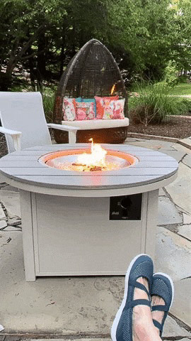 Live photo shot of fire pit with flames and a woman's feet in the foreground.