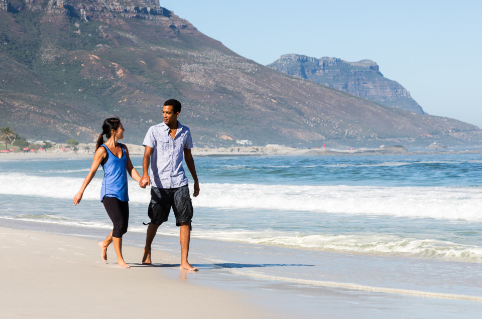Couple walking on beach with mountains behind them in Camps Bay, South Africa