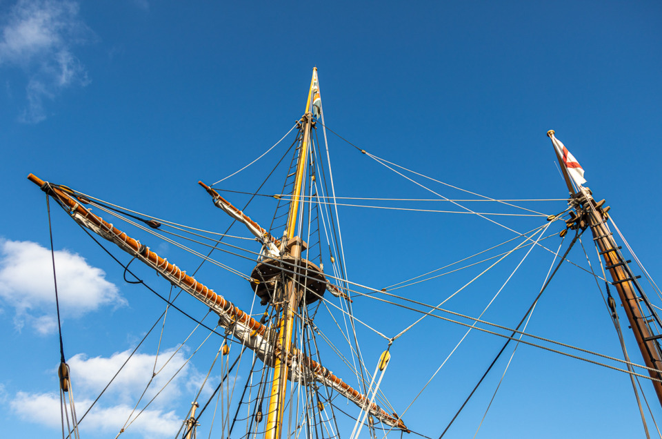 Photo of the rigging of a re-creation sailing ship in Jamestown Settlement, Virginia, against a blue sky with white fluffy clouds.